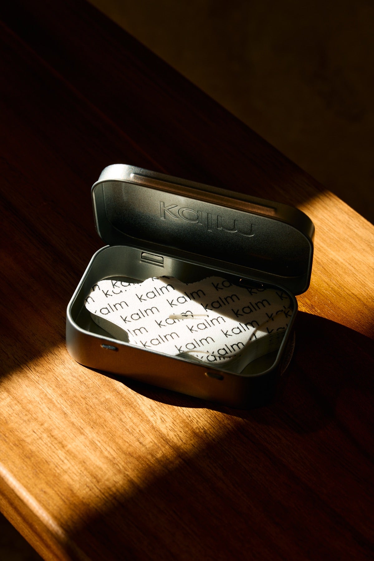 Open KALM travel capsule and strip arranged on warm wood in directional light.