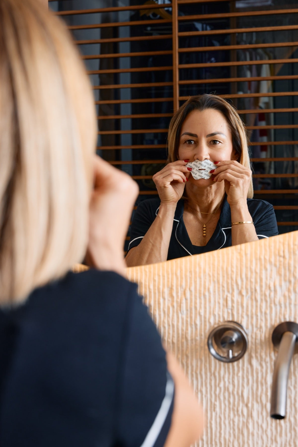 Woman placing a KALM strip over closed lips in front of a mirror.